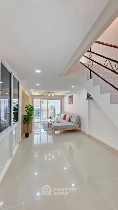 Modern living room with sleek staircase and large windows, featuring stylish decor and ample natural light.