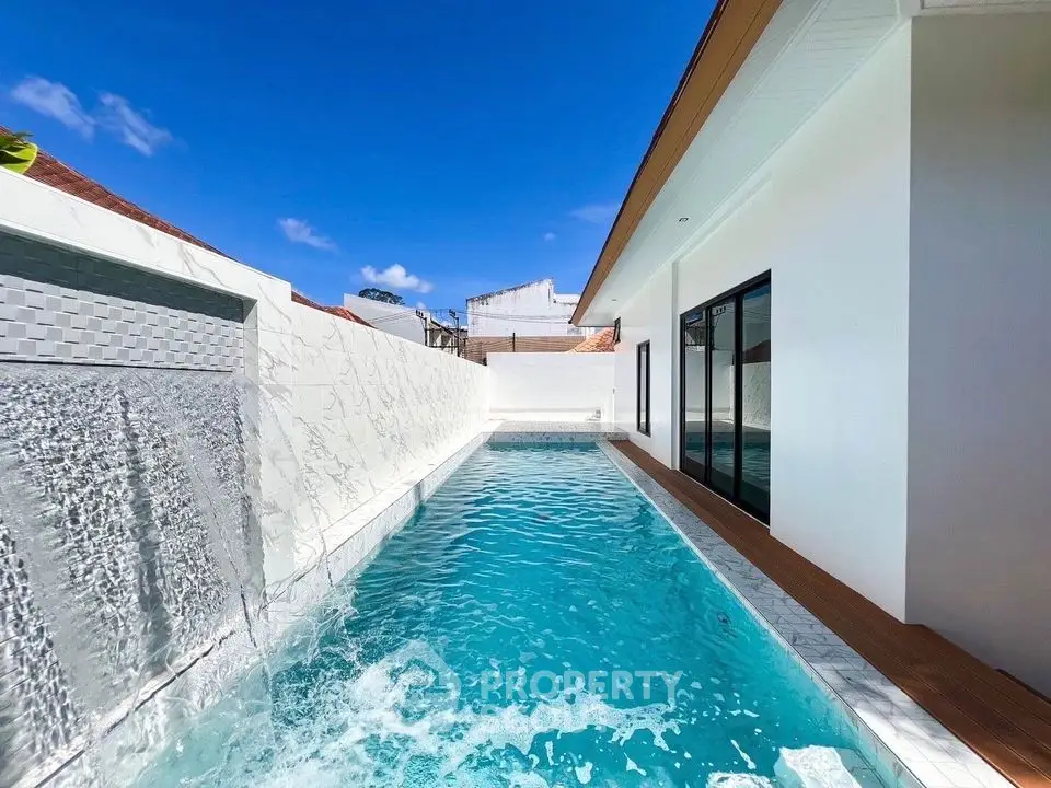 Luxurious modern villa with private pool and waterfall feature under clear blue sky.