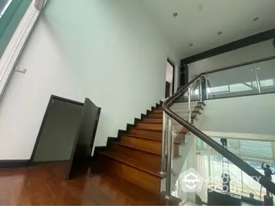 Modern staircase with wooden steps and glass railing in a spacious home interior