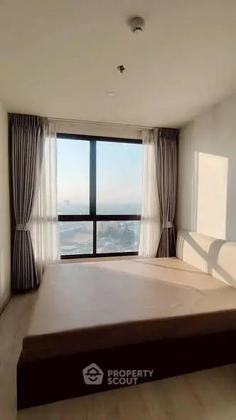 Spacious bedroom with large window offering stunning city view and natural light.