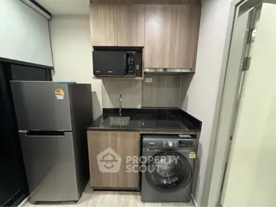 Modern kitchen with sleek appliances including fridge, microwave, and washing machine in compact layout.
