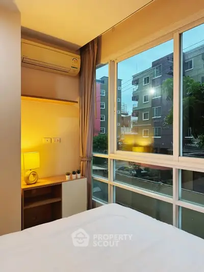 Cozy bedroom with large window offering urban view and natural light.