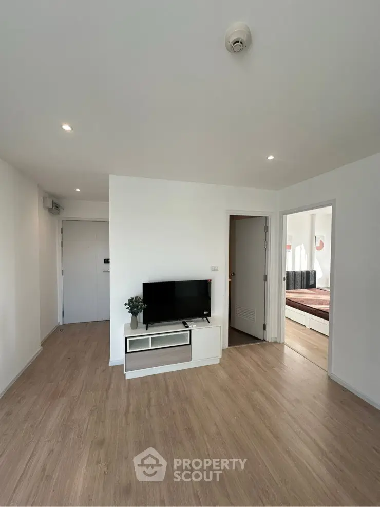 Modern living room with wooden flooring and sleek TV stand, leading to a cozy bedroom.
