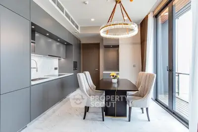 Sleek modern kitchen with integrated appliances and a stylish dining area featuring an elegant chandelier, complemented by natural light from the adjacent balcony.