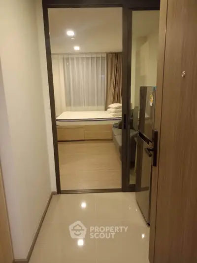 Modern apartment entrance with view into cozy bedroom and sleek fridge