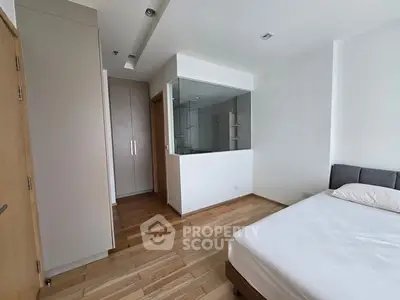 Modern bedroom with wooden flooring and glass partition, featuring a cozy bed and ample storage space.