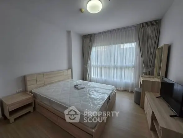 Spacious bedroom with natural light, modern furnishings, and large window in a stylish apartment.