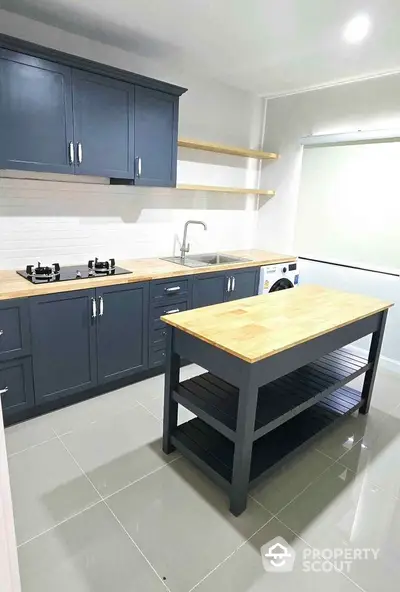 Modern kitchen with sleek cabinetry and island, featuring gas stove and washing machine.