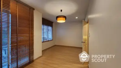 Spacious empty room with wooden flooring and large windows with blinds