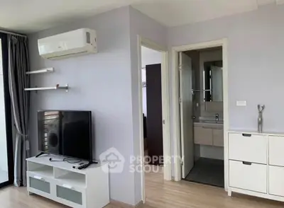 Modern living room with TV and air conditioning, adjacent to a compact bathroom.