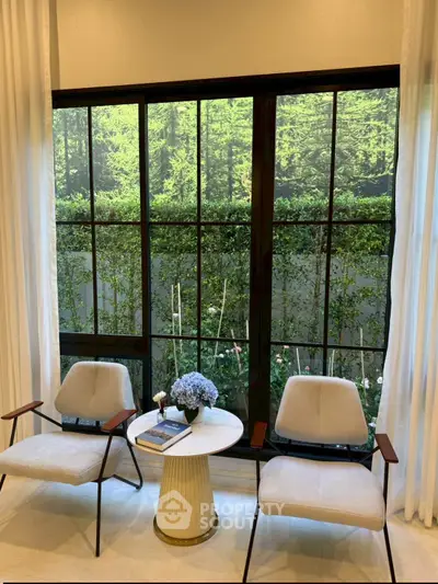 Elegant living room with large window view of lush garden, featuring modern chairs and a stylish side table.