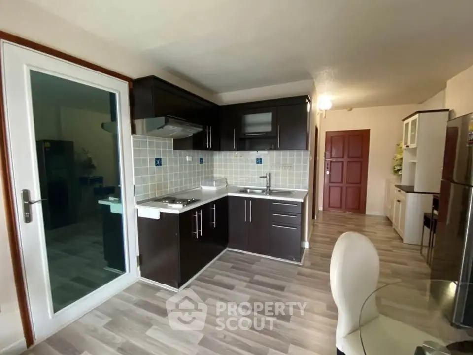 Modern kitchen with dark cabinets and sleek flooring in open layout apartment.