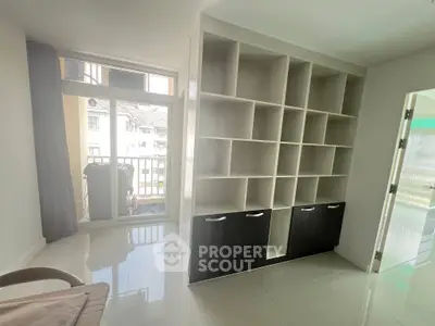 Modern living room with built-in shelving and balcony access, featuring sleek design and ample natural light.