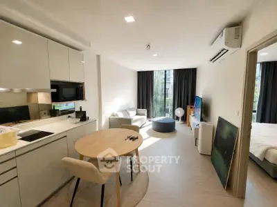 Modern open-plan living room with kitchen, dining area, and bedroom view in a bright apartment.