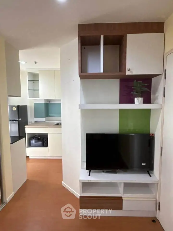 Modern apartment interior with compact kitchen and living area featuring built-in TV unit.