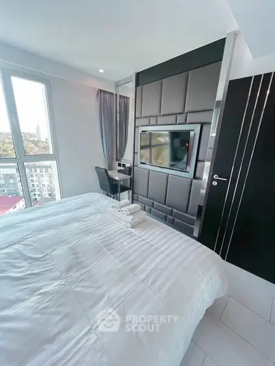 Modern bedroom with sleek design and city view, featuring a wall-mounted TV and cozy workspace.
