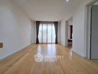 Spacious empty living room with wooden flooring and large window with curtains.