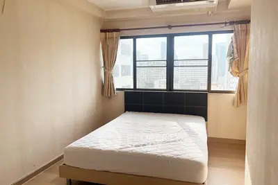 Bright bedroom with large window and city view, featuring a comfortable bed and neutral decor.
