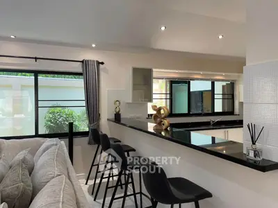 Modern kitchen with sleek black countertops and bar stools, open layout design, and large windows for natural light.