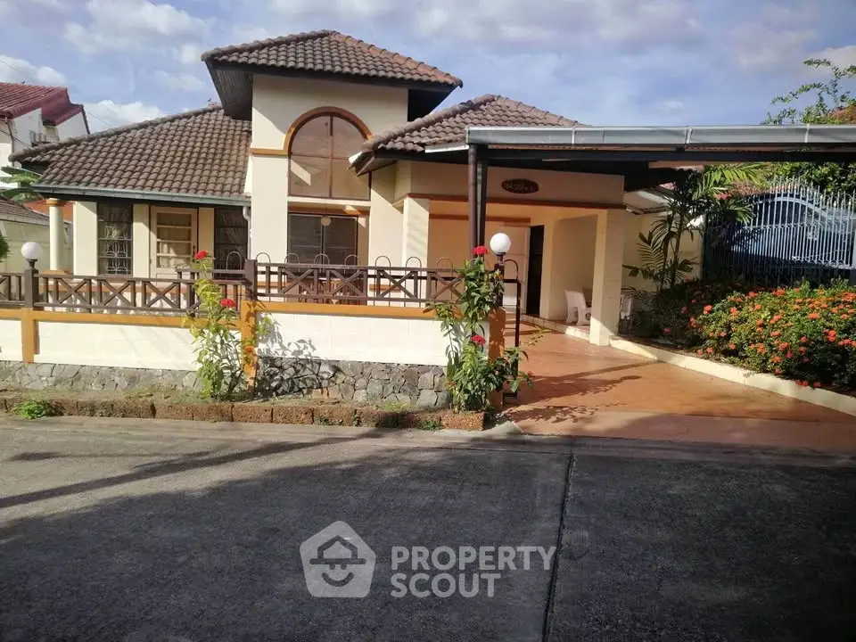 Charming suburban house with a tiled roof and spacious driveway, surrounded by lush greenery and vibrant flowers.