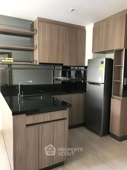 Modern kitchen with sleek black countertops and stainless steel fridge in a stylish apartment.