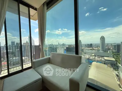 Stunning city view from modern high-rise apartment with floor-to-ceiling windows and cozy seating area.