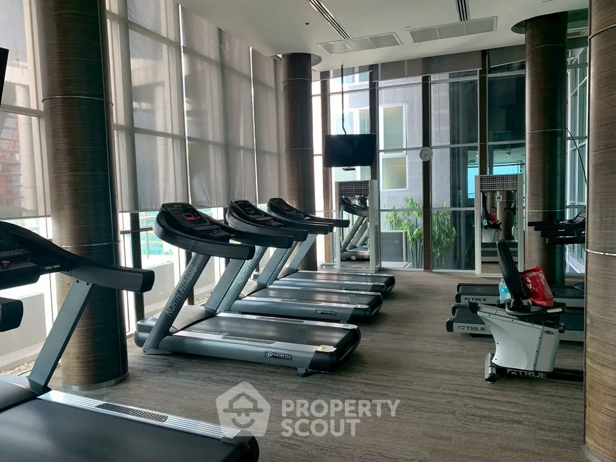 Modern gym with state-of-the-art equipment and large windows in luxury residential building.