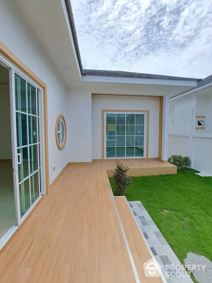 Modern home exterior with sliding glass doors and lush green lawn under a partly cloudy sky.