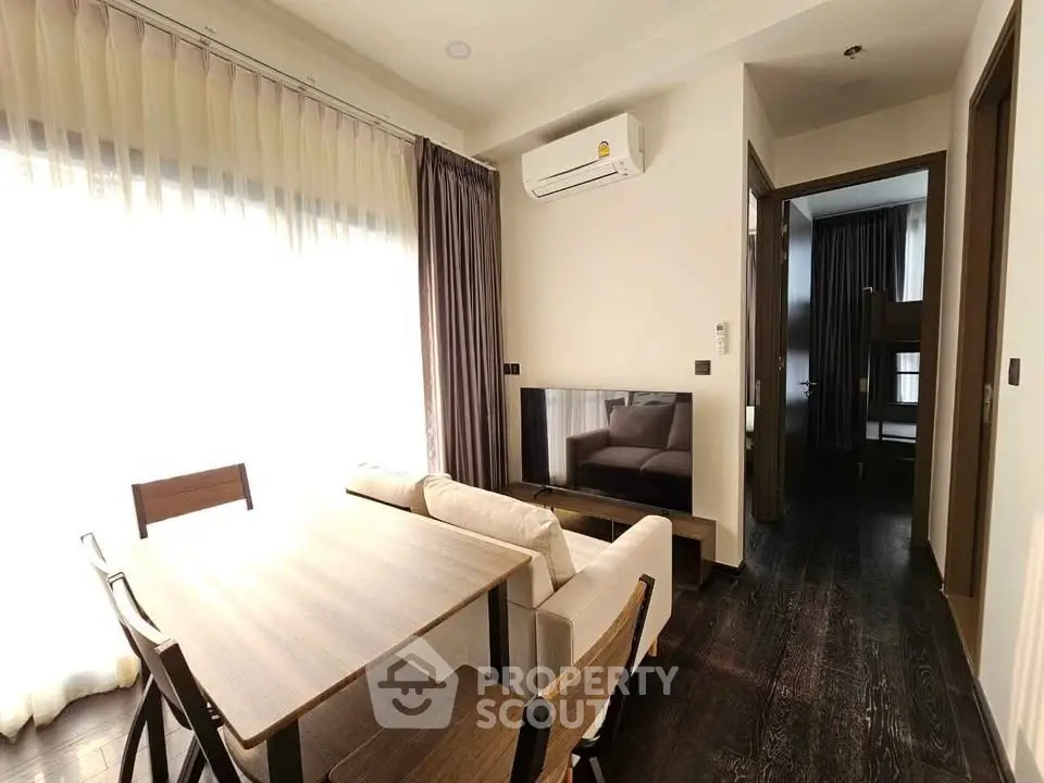 Modern living room with dining area and natural light, featuring sleek furniture and air conditioning.
