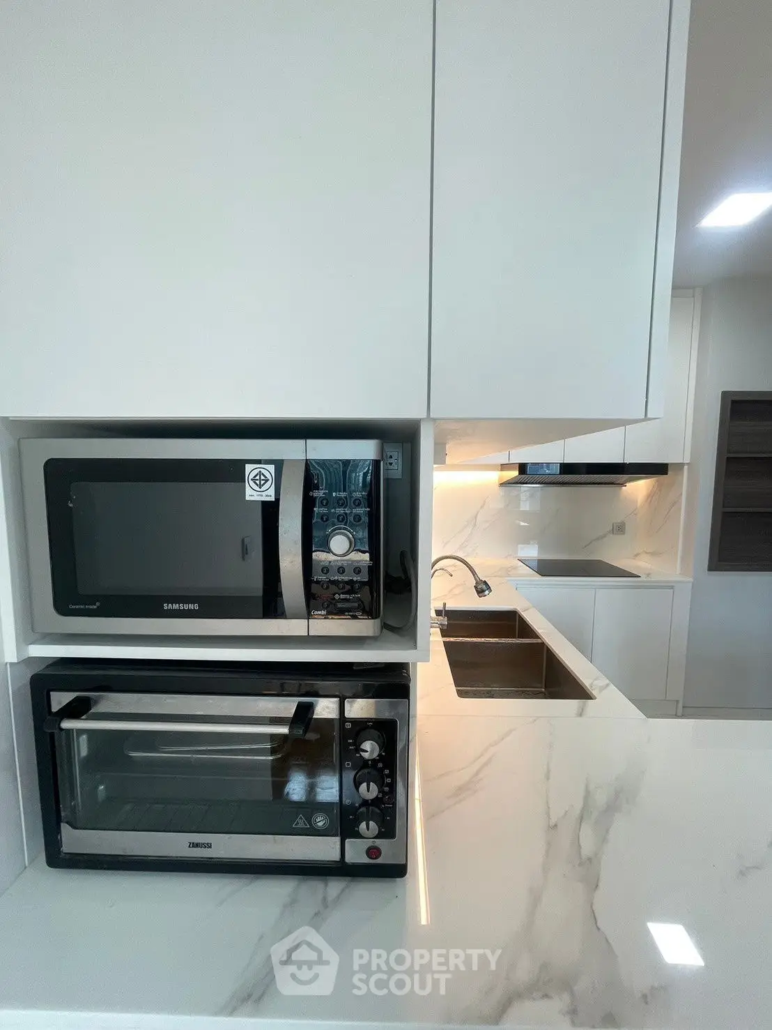 Modern kitchen with sleek appliances and marble countertops, featuring a built-in microwave and oven.