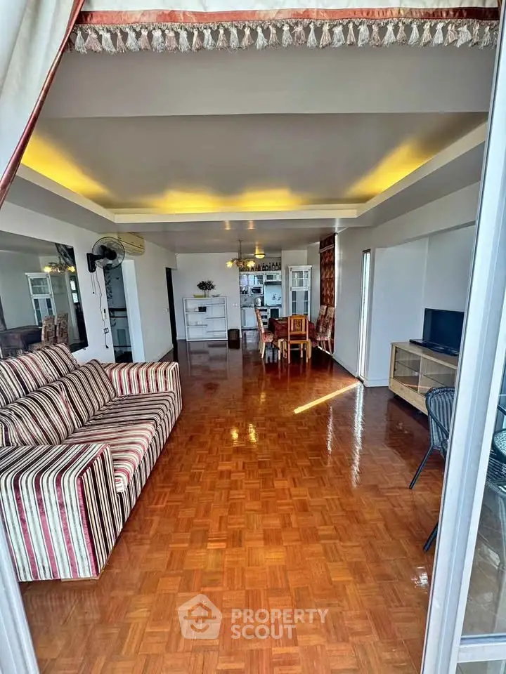 Spacious living room with stylish decor and parquet flooring, leading to a dining area.