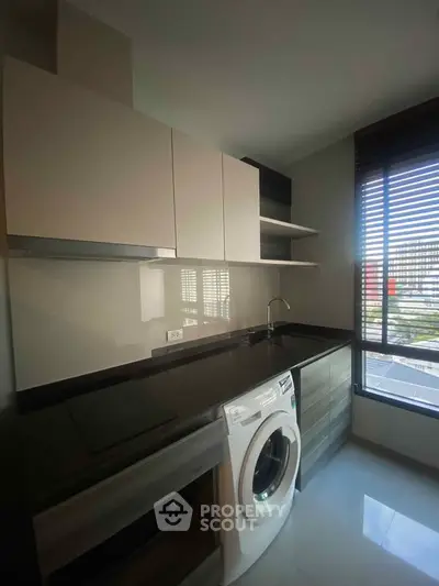 Modern kitchen with sleek cabinets and built-in washing machine, featuring large window for natural light.