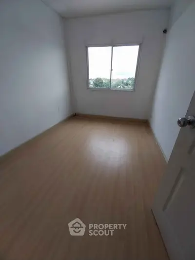 Spacious empty room with wooden flooring and large window offering natural light.