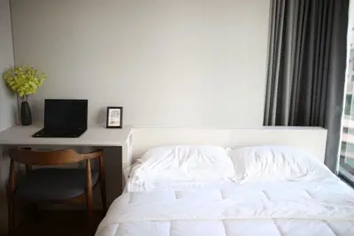 Modern bedroom with cozy bed, work desk, and large window offering natural light.