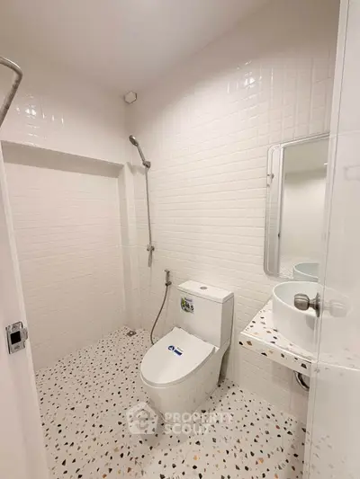 Modern bathroom with sleek white tiles and terrazzo flooring, featuring a stylish toilet and shower area.
