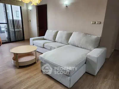 Spacious living room with modern sofa and round coffee table, featuring wooden flooring and balcony access.