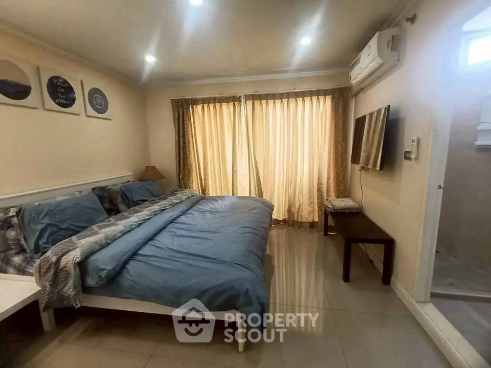 Cozy bedroom with large bed, wall-mounted TV, and natural light from curtains.