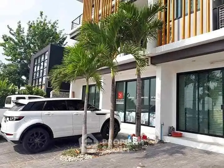 Modern townhouse exterior with palm trees and parked luxury SUV, showcasing contemporary architecture and urban living.