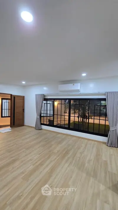 Spacious living room with large windows and wooden flooring, offering a serene garden view.
