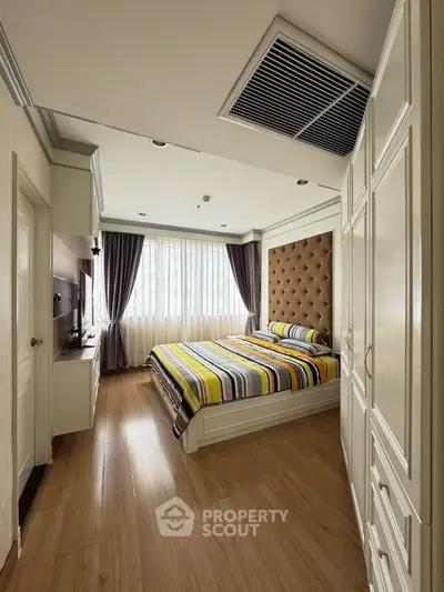 Elegant bedroom with striped bedding, large window, and ample storage in a modern apartment.