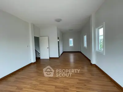Spacious empty room with wooden flooring and large windows, perfect for customization.