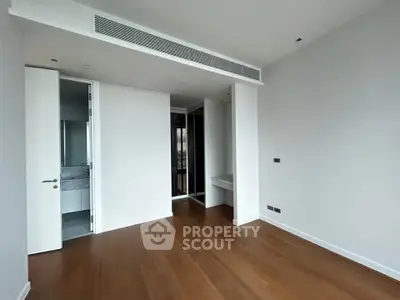 Spacious modern bedroom with wooden flooring and sleek design in a luxury apartment.