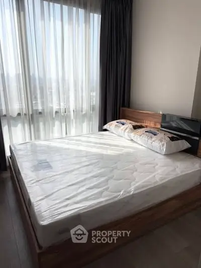 Spacious bedroom with large window and modern bed frame, offering ample natural light and city views.