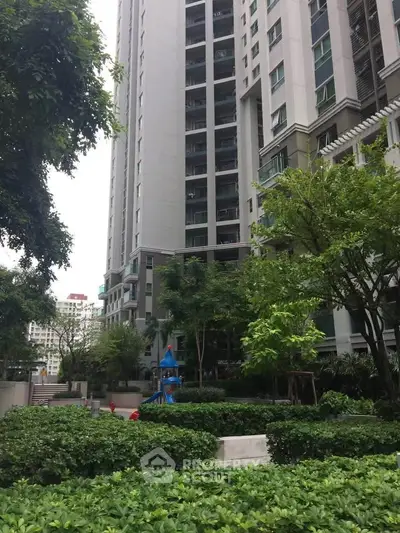 Modern high-rise building with lush green garden and playground area.