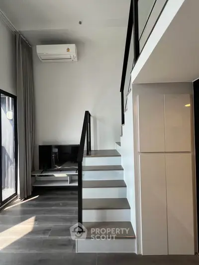 Modern duplex interior with sleek staircase and air conditioning unit, featuring stylish design and ample natural light.
