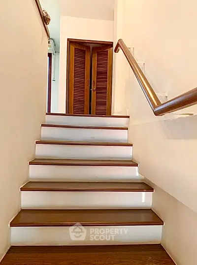 Elegant wooden staircase with sleek handrail leading to a stylish interior door, perfect for modern homes.