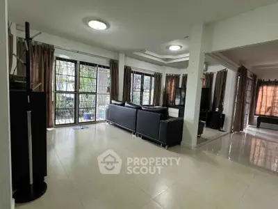 Spacious living room with modern black leather sofas and large windows offering natural light.