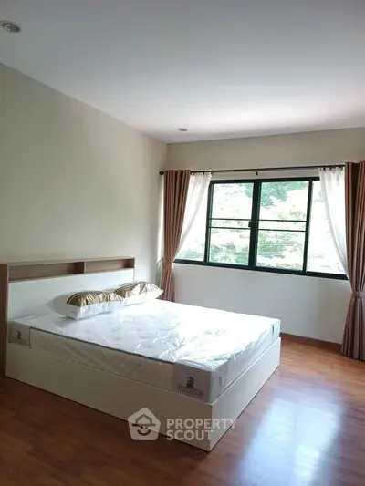 Spacious bedroom with large window and wooden flooring, perfect for natural light lovers.