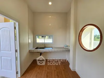 Bright kitchen with wooden flooring and a round mirror, featuring a sleek countertop and window view.