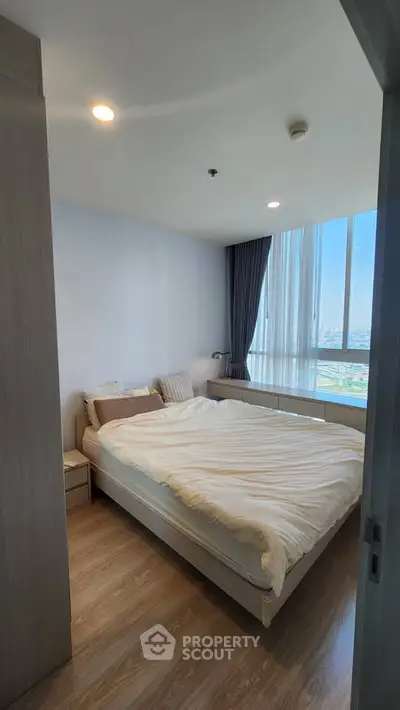 Bright and cozy bedroom with large window offering stunning city views, perfect for relaxation.